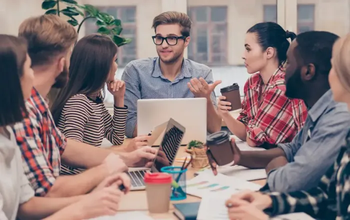 Team von jungen Fachleuten bei einer Besprechung im Büro, diskutieren und arbeiten an Laptops.